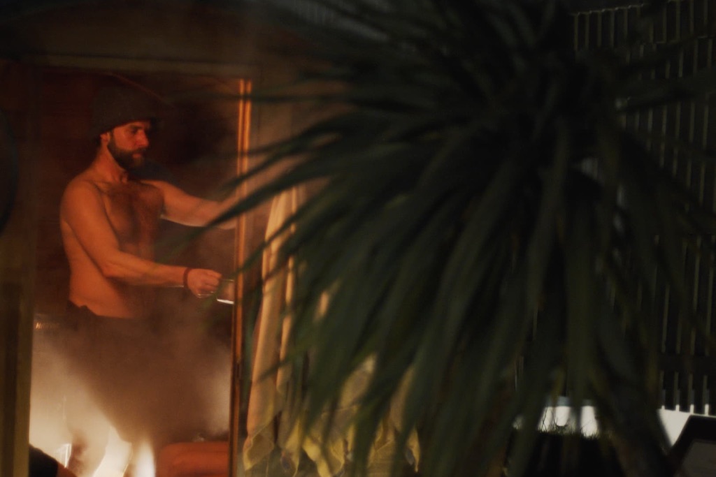 From outside the sauna we see Nick T guiding a sauna ritual using salt inhalations on the participants