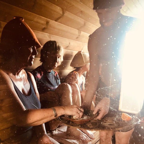 A group of women are doing a sauna ritual. the sauna master is offering them orange and body scrubs for a nourishing bathing experience