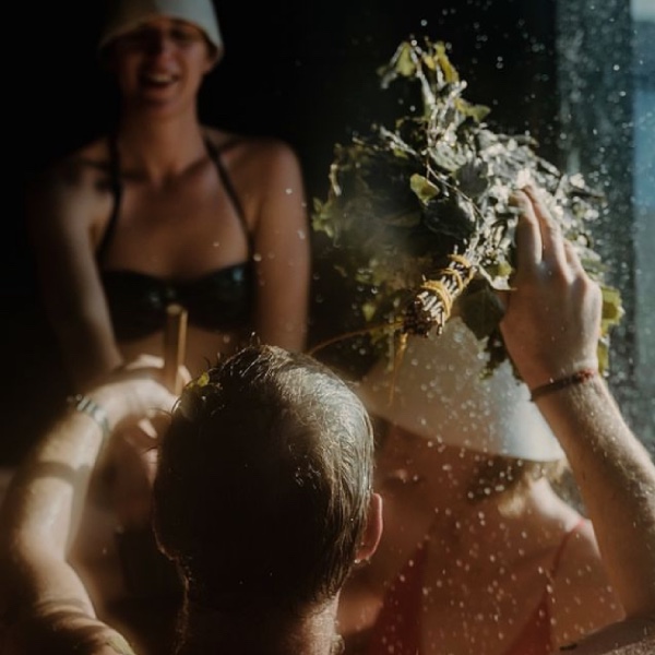 A group of people enjoying a sauna ritual. The sauna master, Nick T, uses sauna whisks to move the steam and the heat around the sauna